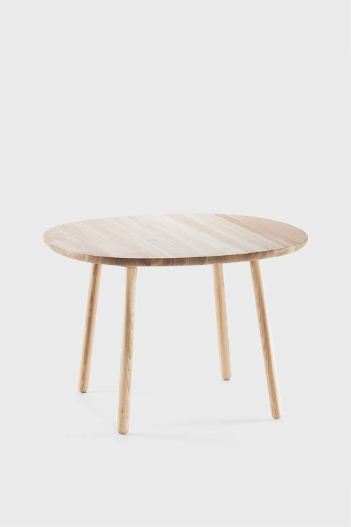 Naïve Dining Table with a round, oiled ash surface and four natural wood legs, showcasing a simple and clean design.