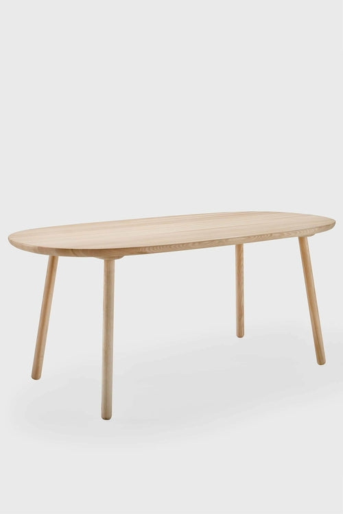 Lightly oiled wooden Naïve Dining Table with an oval tabletop and slender legs, showcasing a modern, minimal design.