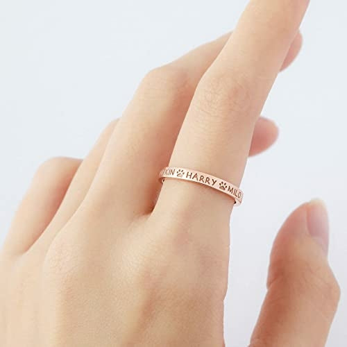 Personalized rose gold ring worn on a finger, engraved with pet names and small paw prints in between.
