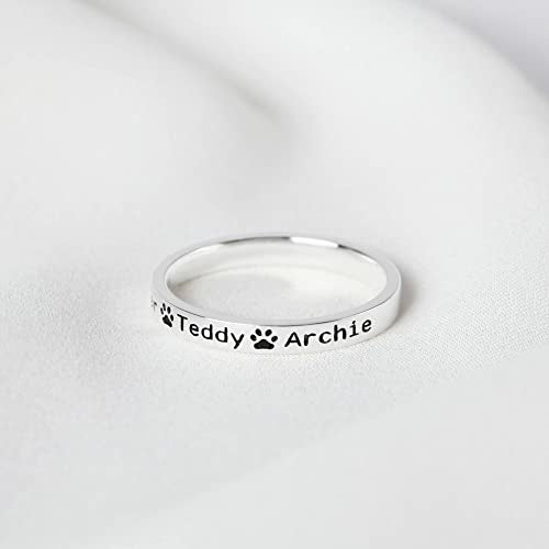 Custom silver ring features the names "Teddy" and "Archie" with a pawprint design in between, resting on soft fabric.