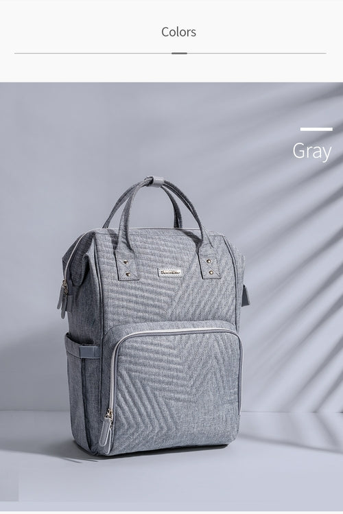 Gray quilted diaper bag backpack with dual zippers, adjustable padded straps, and a large front pocket.
