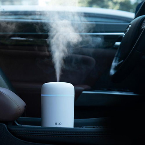 Portable white air humidifier and aroma diffuser with mist rising, placed in a car's center console.