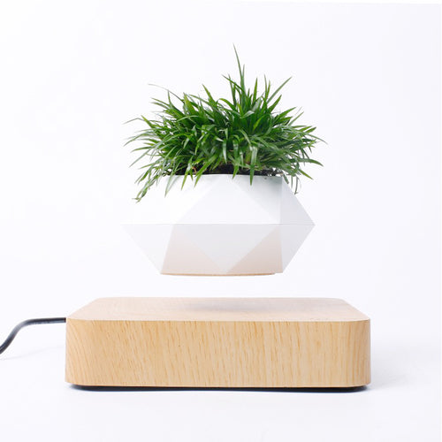 Levitating flowerpot in a white geometric design, floating above a light wood base with grass-like greenery inside.