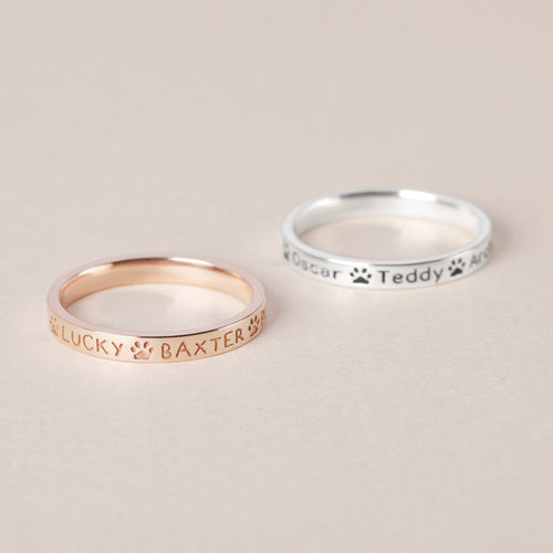 Custom rings featuring engraved names; one in rose gold with "LUCKY BAXTER" and one in silver with "Oscar Teddy Amy.