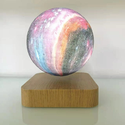 Floating moon lamp with a colorful, textured surface, supported by a square wooden base, softly illuminated.