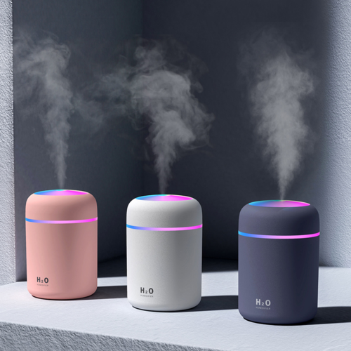 Three portable air humidifier aroma essential oil diffusers in pink, white, and dark gray with colorful mist emitting from each.