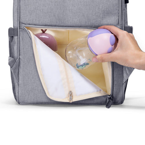 A hand reaches into the zippered pocket of a gray Modern Quilted Diaper Bag Backpack, revealing a bottle and a small toy.