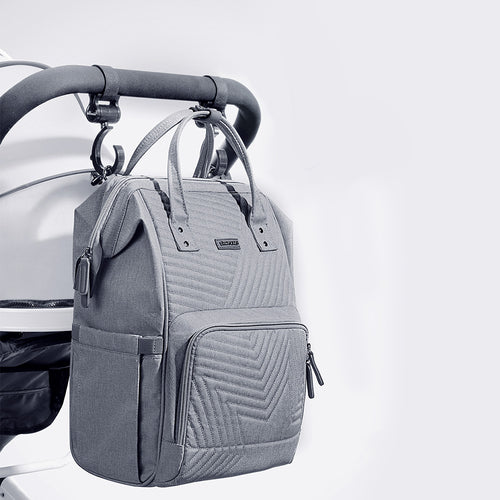 Gray quilted diaper bag backpack with dual top handles, D-ring buckles, and front zippered pocket, hanging from stroller.